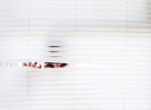 Man peeking through white blinds looking at the camera